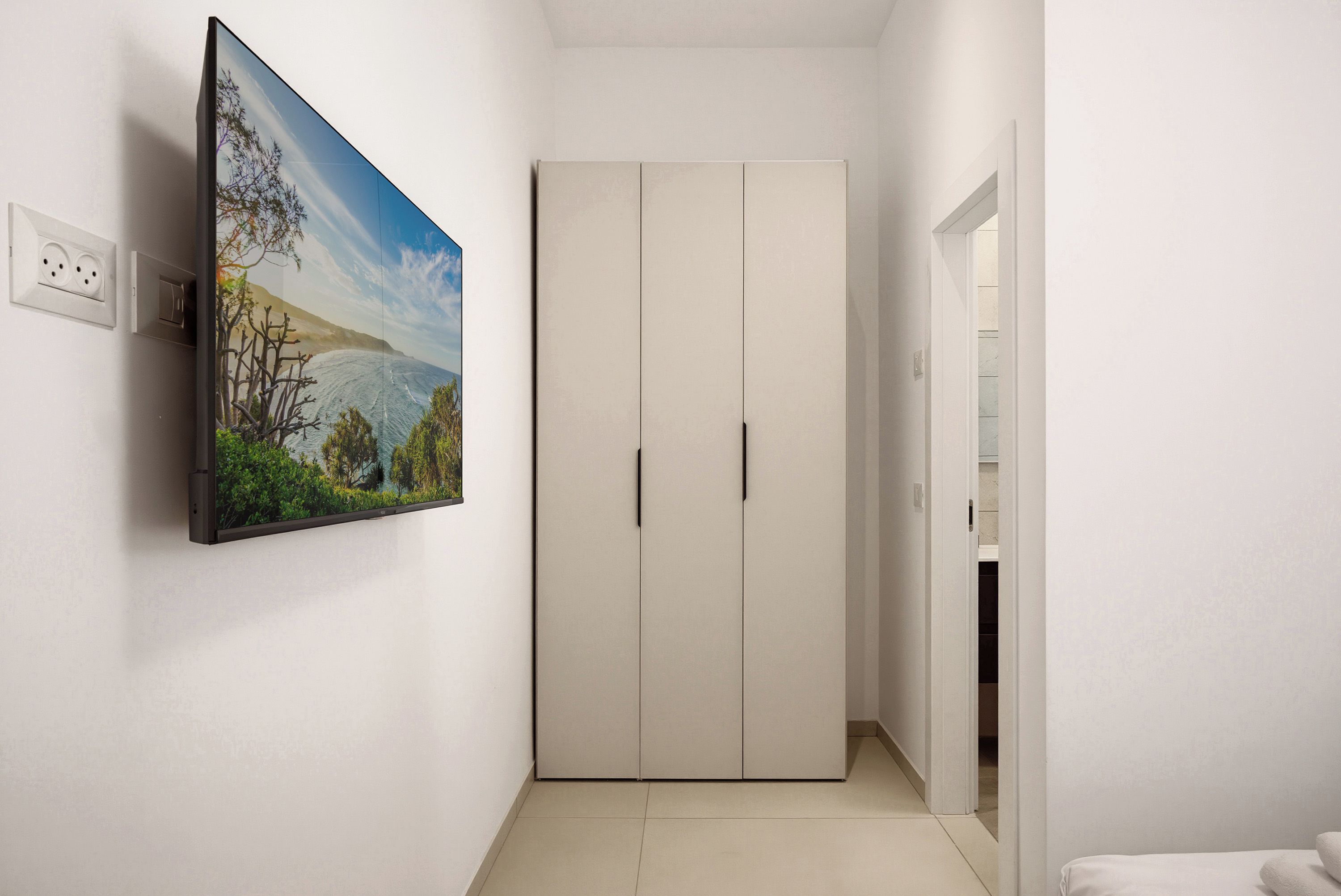 A hallway with a white wardrobe, a painting on the wall, and a door leading to another room.