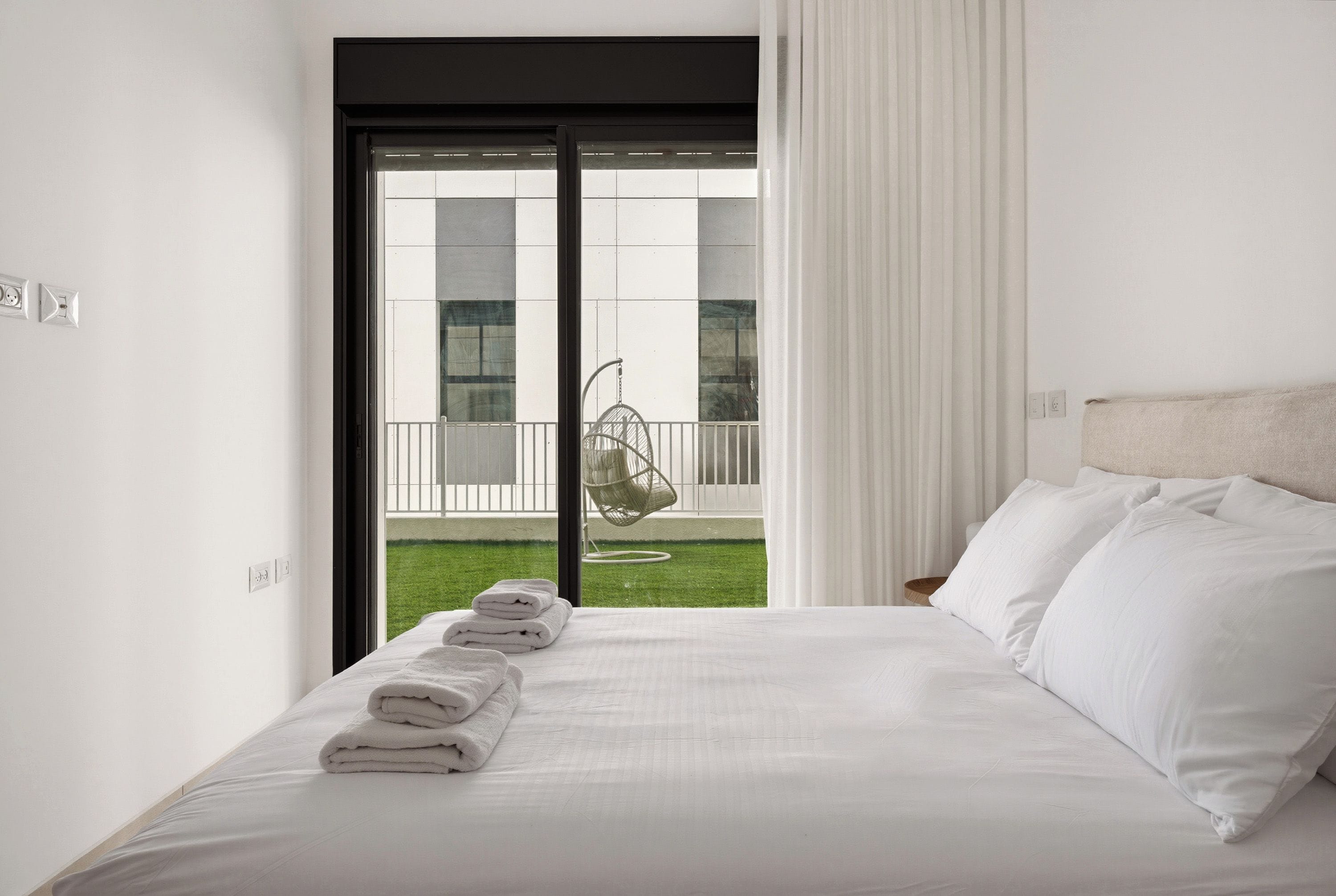 A hotel room with a bed, a balcony with a hanging chair, and a view of a building.