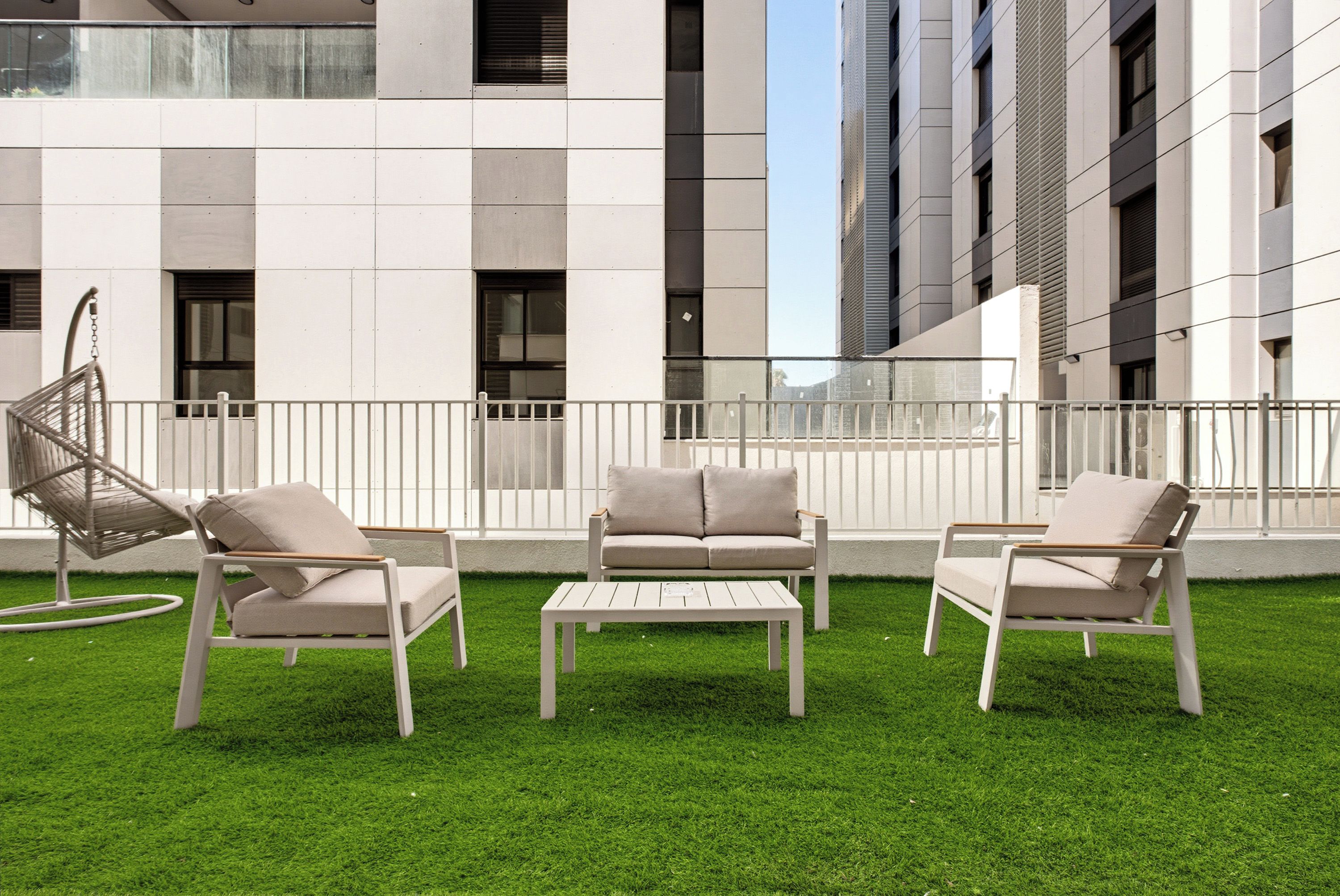 An outdoor seating area with a sofa and two chairs, a small table, and a hanging chair.