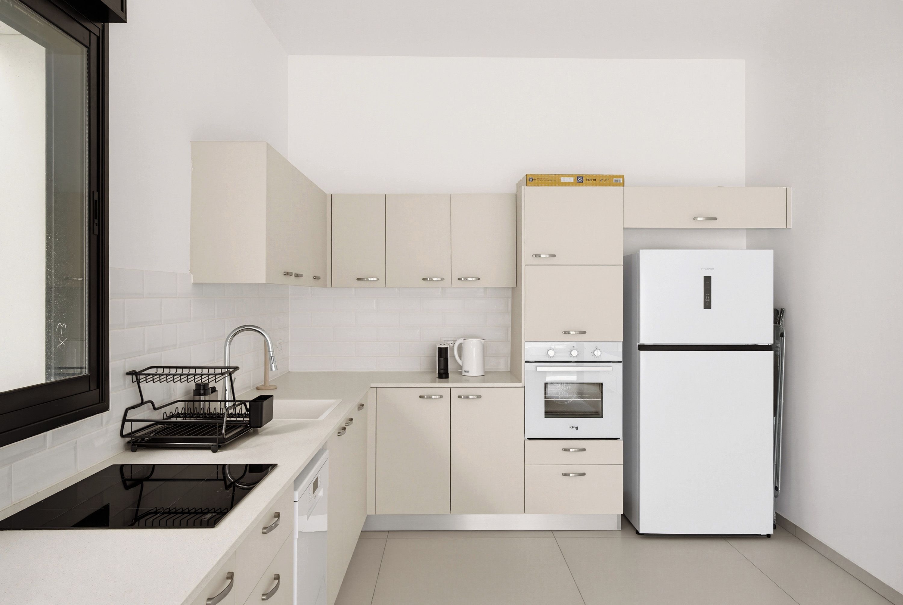 A modern kitchen with white cabinetry, a built-in oven, a refrigerator, and a dish drying rack.