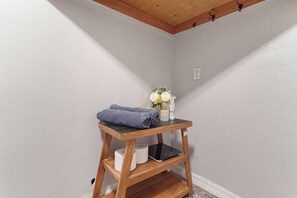 A corner of a room with a wooden shelf holding a towel, toilet paper, and a small vase with flowers. - Your Ybor Base - WFH Pet Friendly - Full Kitchen (Tampa)