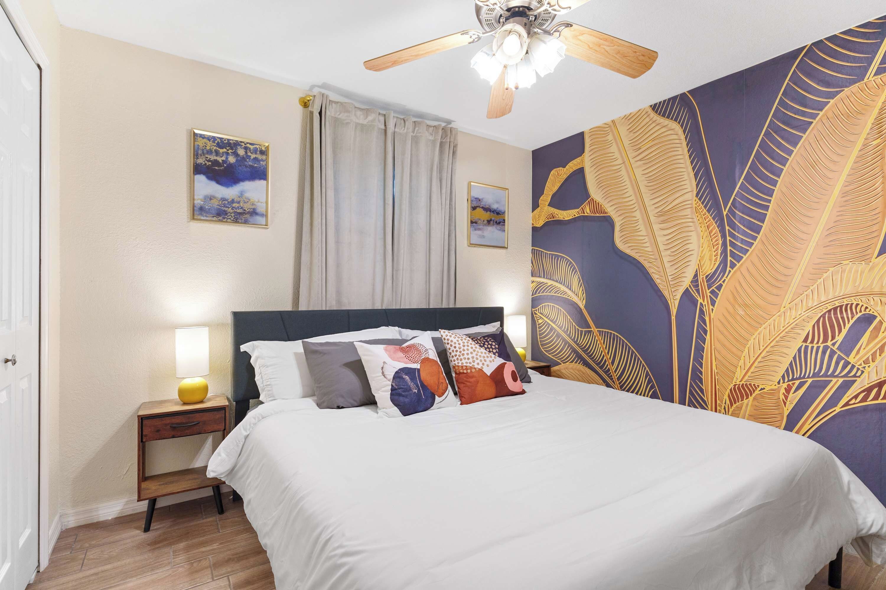 A bedroom with a bed, a nightstand, a ceiling fan, and a wall with a large leaf pattern.