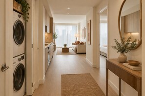 A modern interior with a laundry area, a sofa, a coffee table, and a console table with a mirror and vase.