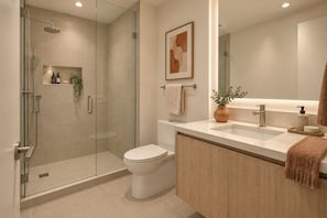 Un baño moderno con ducha envuelta en vidrio, inodoro, lavamanos con espejo y toallero.