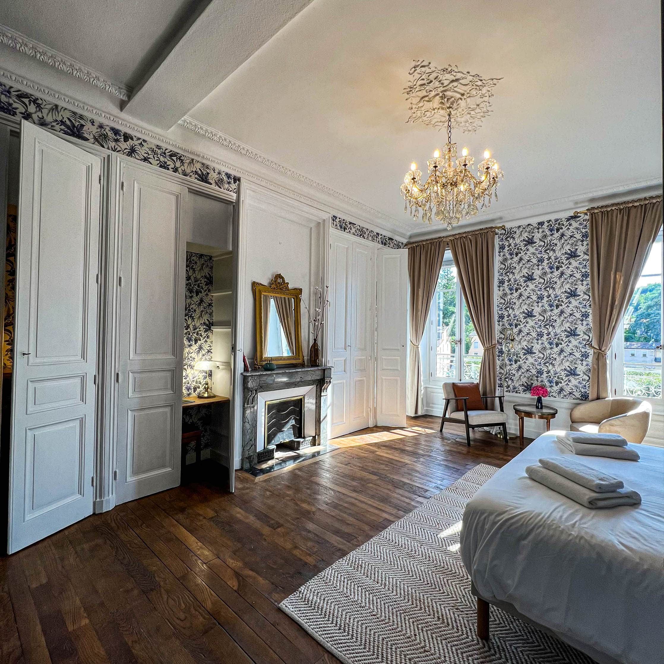 Une chambre spacieuse avec un grand lit, une cheminée, un lustre et une vue sur l’extérieur.