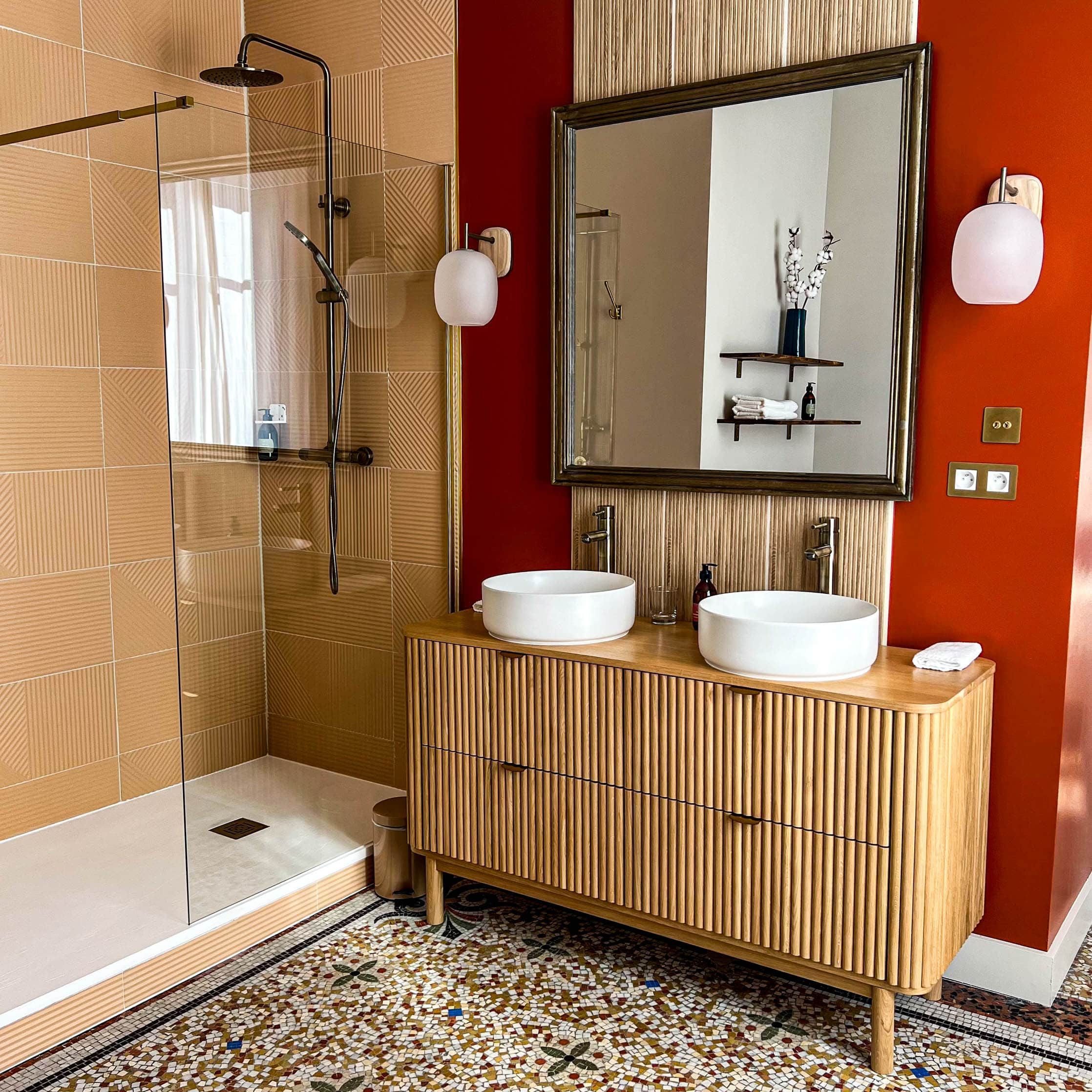 Une salle de bain moderne avec une douche à parois de verre, deux lavabos, un grand miroir et un sol carrelé.