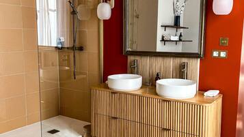 Une salle de bain moderne avec une douche à parois de verre, deux lavabos, un grand miroir et un sol carrelé.