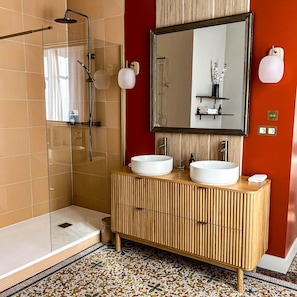 Ein modernes Badezimmer mit Duschkabine aus Glas, zwei Waschbecken, einem großen Spiegel und einem Fliesenboden.