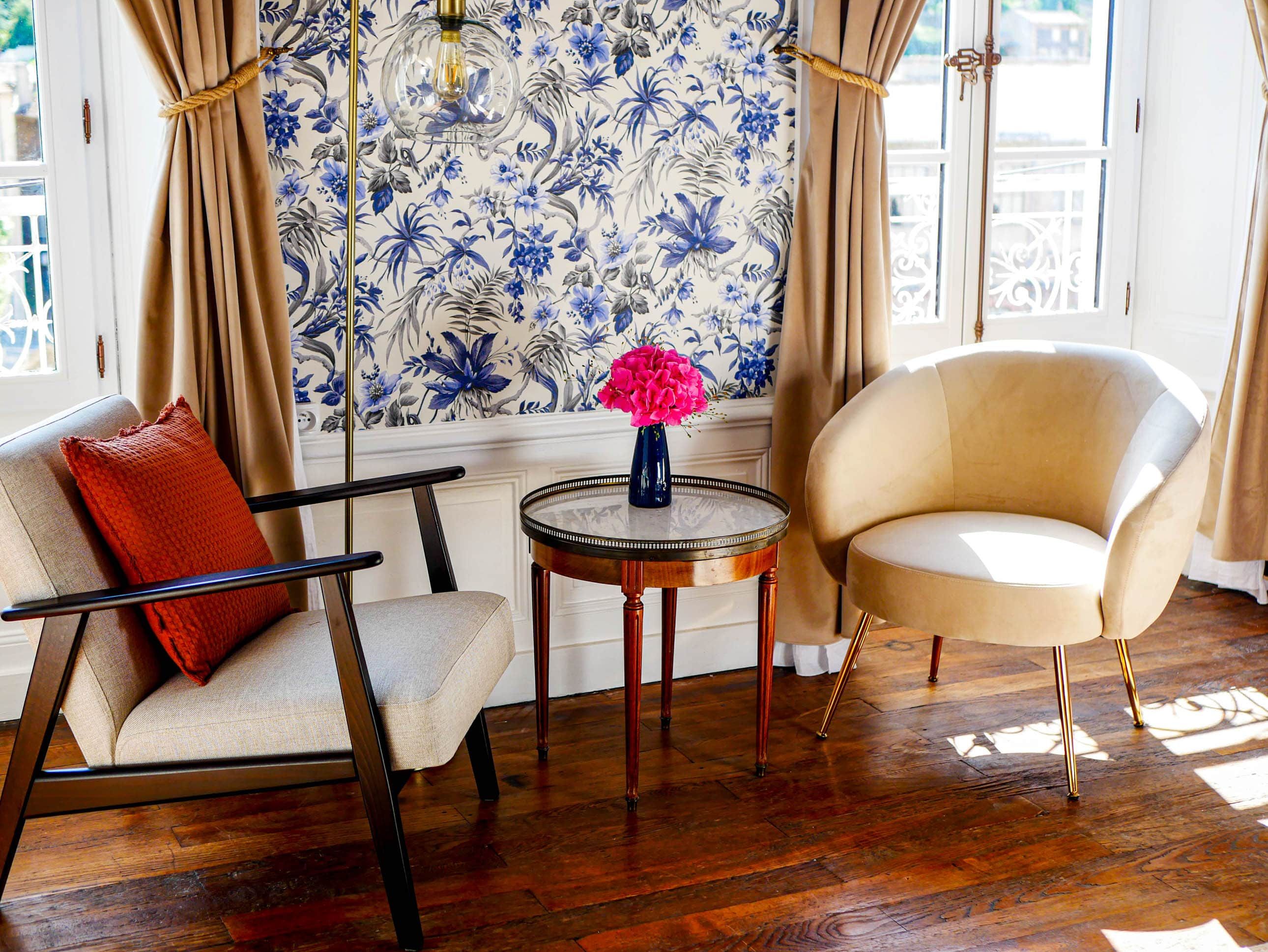 Une pièce comprenant un canapé, un fauteuil, une table ronde et un papier peint à motifs floraux.