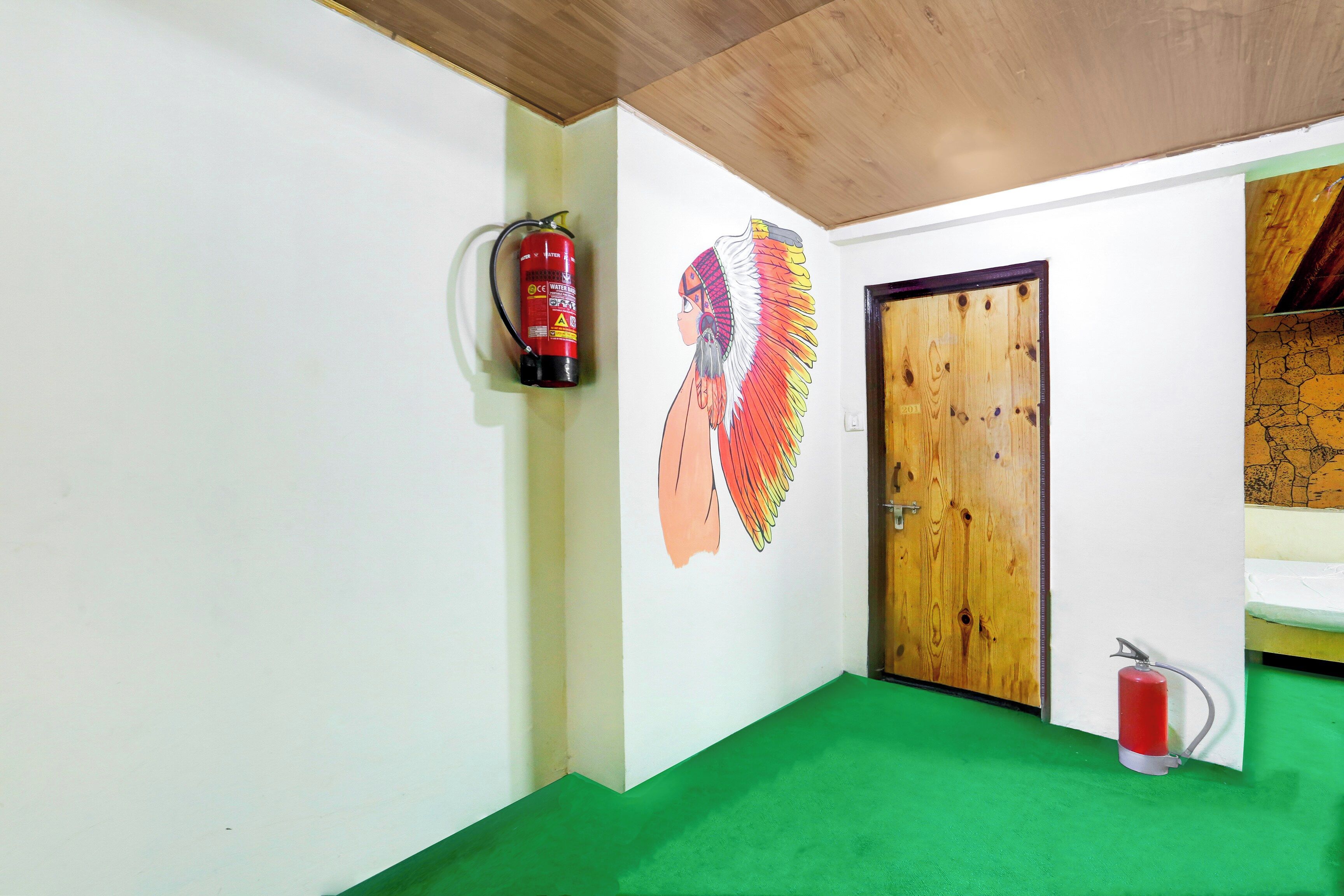 A room with a green carpet, a wooden door, and a fire extinguisher mounted on the wall.