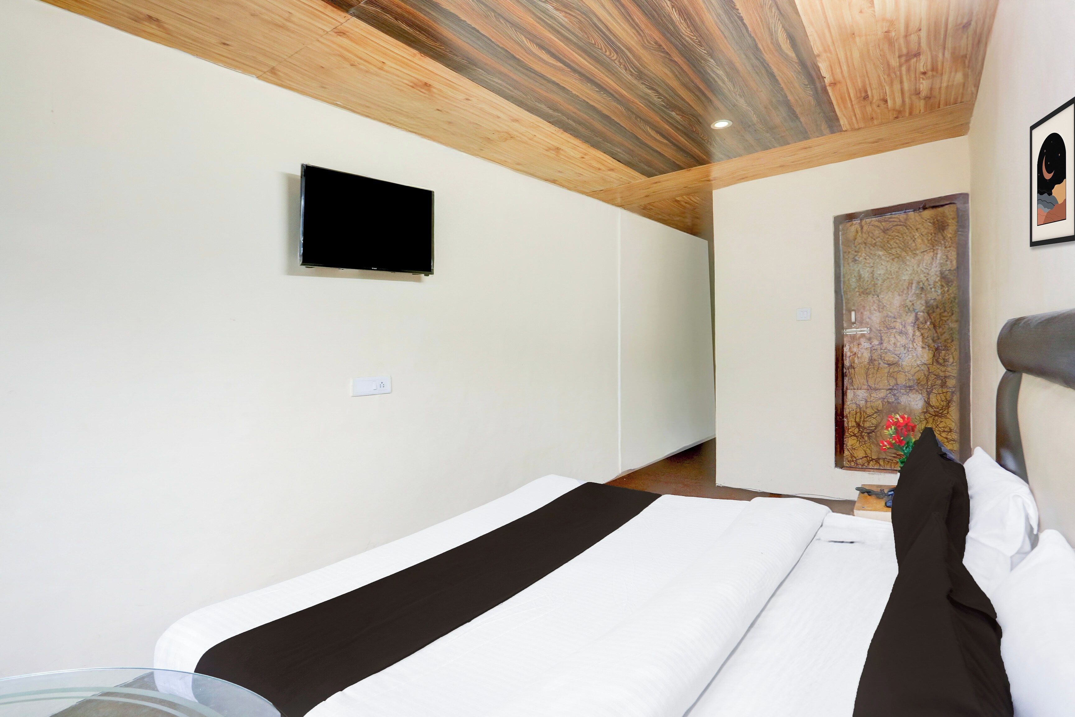 A hotel room with a bed, a television mounted on the wall, and a painting on the wall.