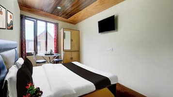 Habitación de hotel con cama, escritorio, silla, televisor y ventana con vista a edificios.
