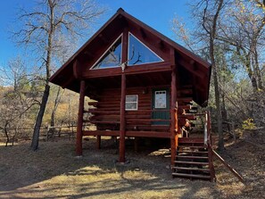 A log cabin with a large front window, a green door, and a staircase leading to the entrance. - The Old West Hideout (Medora)
