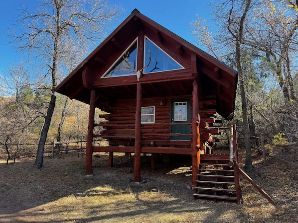 A log cabin with a large front window, a green door, and a staircase leading to the entrance.