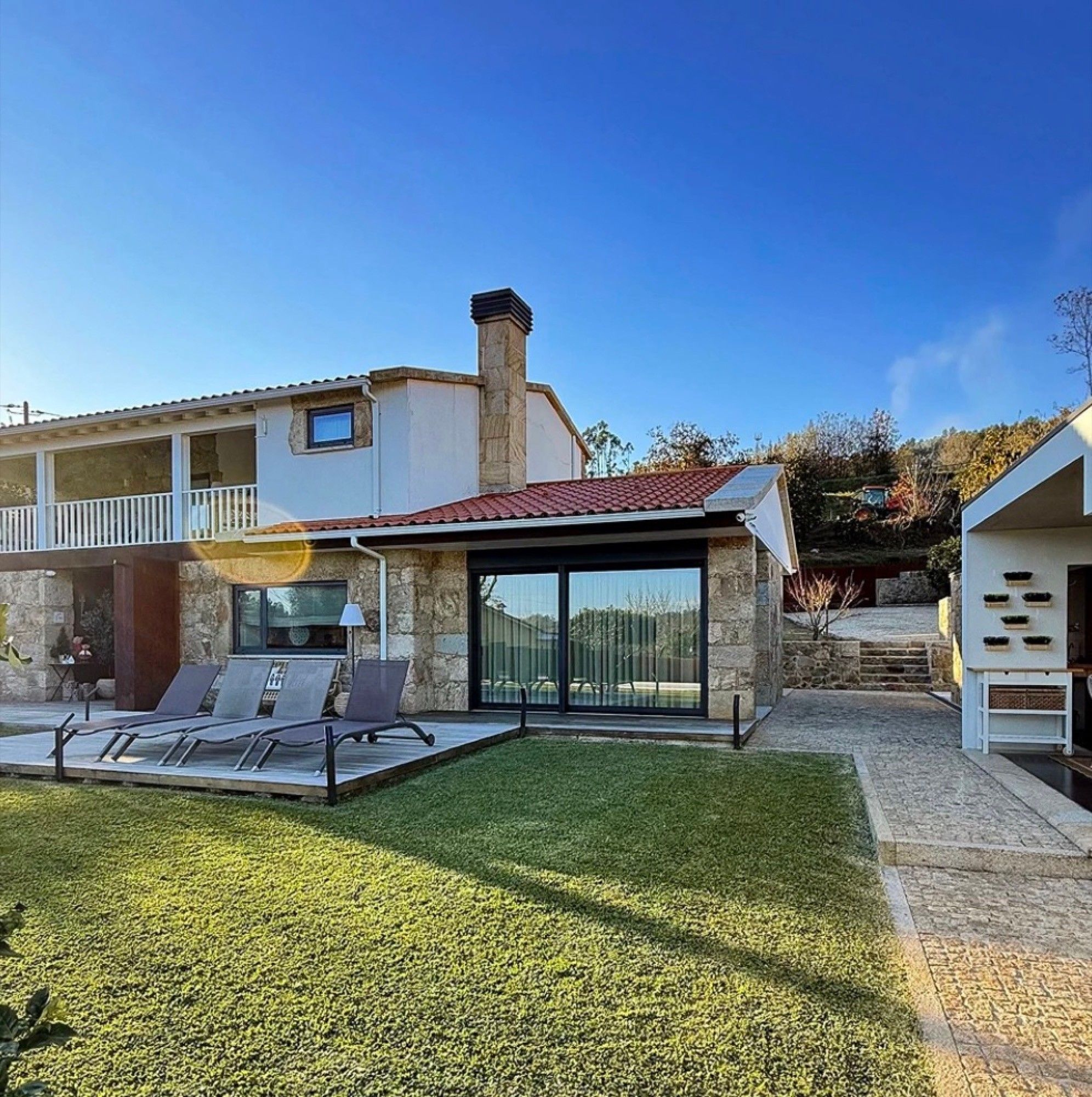 Une maison moderne dotée d’un patio, d’un espace extérieur aménagé et couvert, et d’une cheminée en pierre.