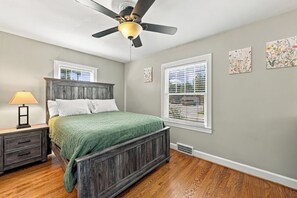 A bedroom with a bed, nightstand, lamp, ceiling fan, and wall art.