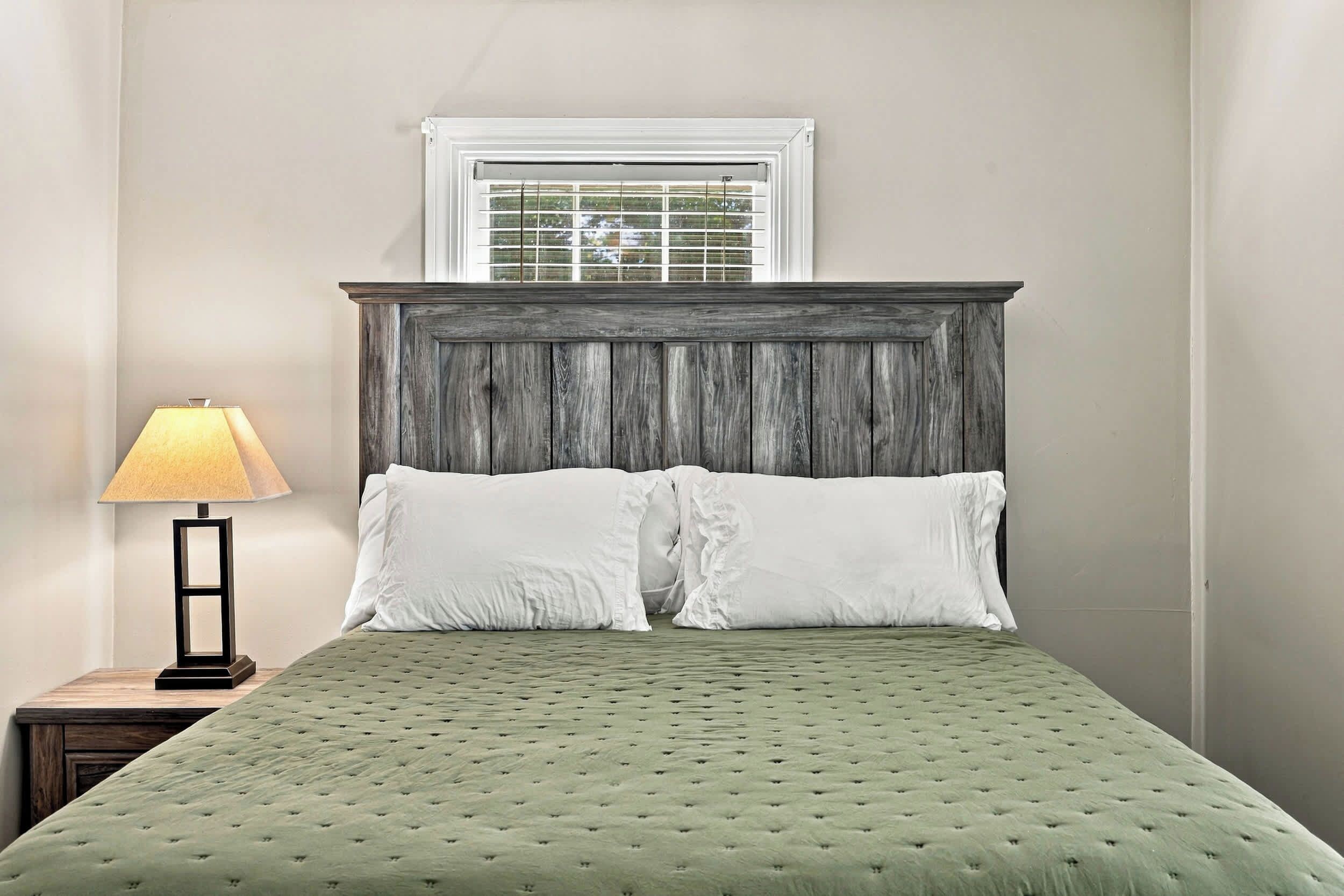 A bed with a green quilt, a wooden headboard, and a window with blinds.