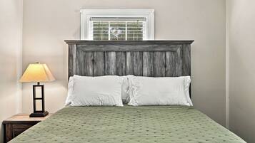 A bed with a green quilt, a wooden headboard, and a window with blinds.