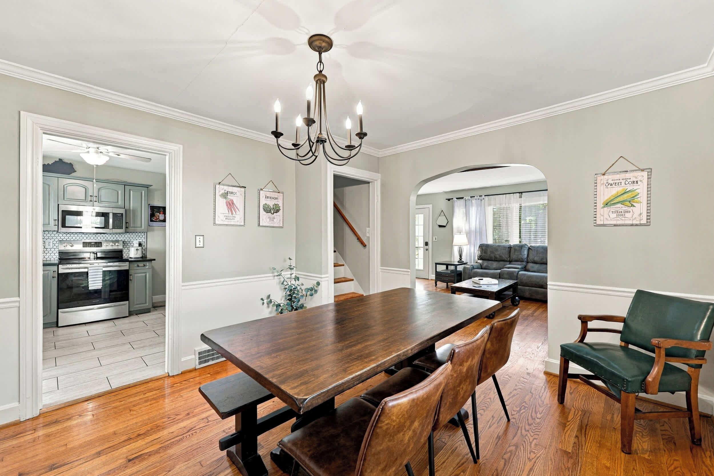 Un comedor con una mesa y sillas de madera, una cocina al fondo y una escalera que lleva a otra habitación.