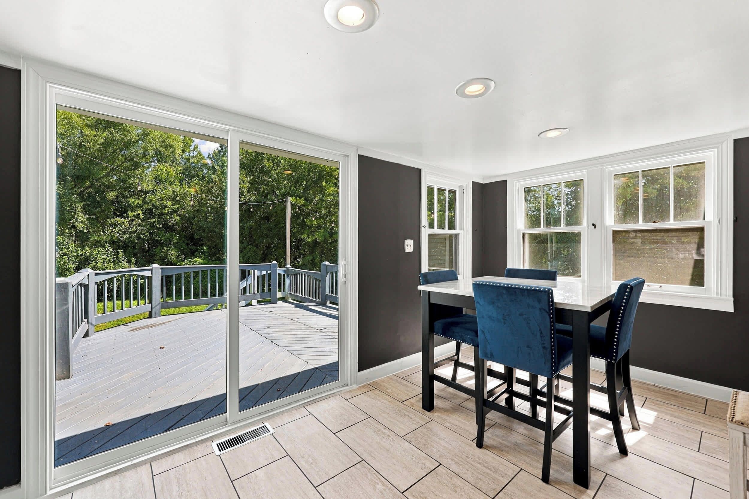 A dining area with a table and chairs, large windows, and a view of a deck and trees.
