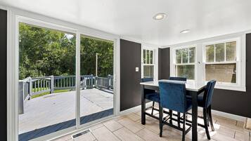 A dining area with a table and chairs, large windows, and a view of a deck and trees.