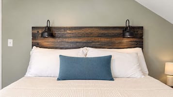 Un lit recouvert d’une couverture blanche texturée, deux oreillers blancs, un coussin décoratif de couleur turquoise et une tête de lit en bois agrémentée de deux lampes fixées au mur.