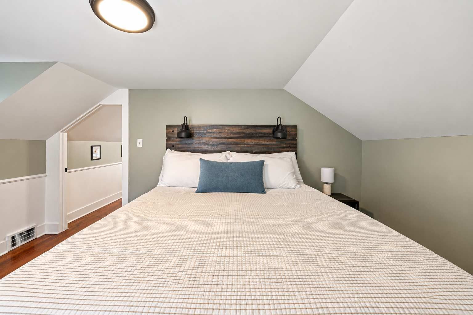 Un dormitorio con techo inclinado, una cama con cabecera de madera, dos lámparas de noche y una mesita de noche.