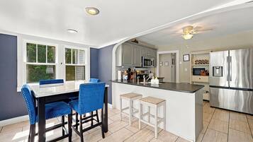 A modern kitchen with a central island, bar stools, and a dining table with blue chairs.
