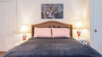 A bedroom with a bed, two bedside lamps, a wall-mounted painting, and a white door.
