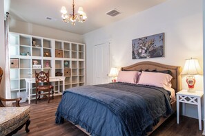 A bedroom with a large bed, a nightstand, a chair, a built-in shelving unit, and a chandelier.