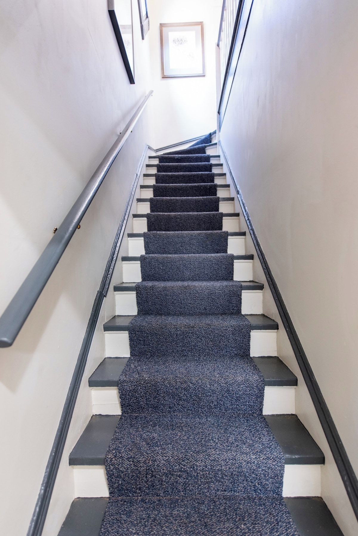 A staircase with a carpeted landing and a handrail on the left.