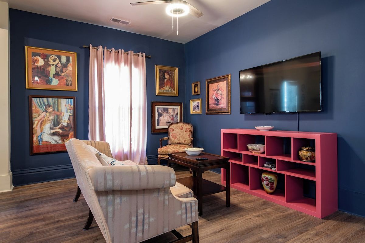 A living room with a sofa, armchair, coffee table, and a pink shelving unit against a blue wall.