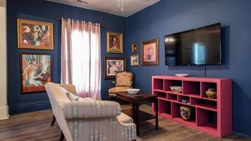 A living room with a sofa, armchair, coffee table, and a pink shelving unit against a blue wall.