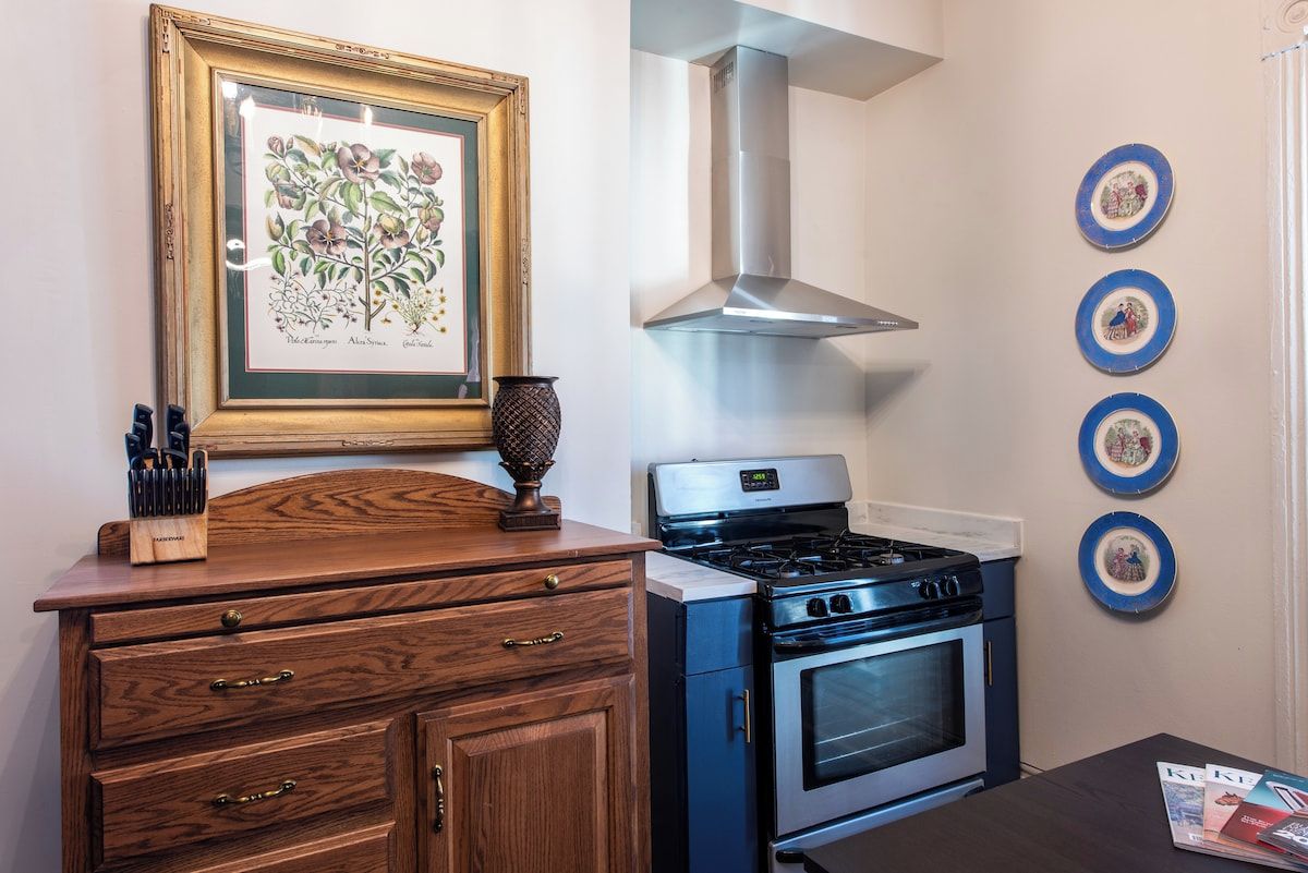 A kitchen with a stove, oven, and a framed botanical illustration on the wall.