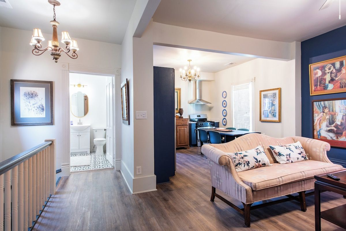 A spacious living area with a sofa, a dining table, and a kitchen in the background.