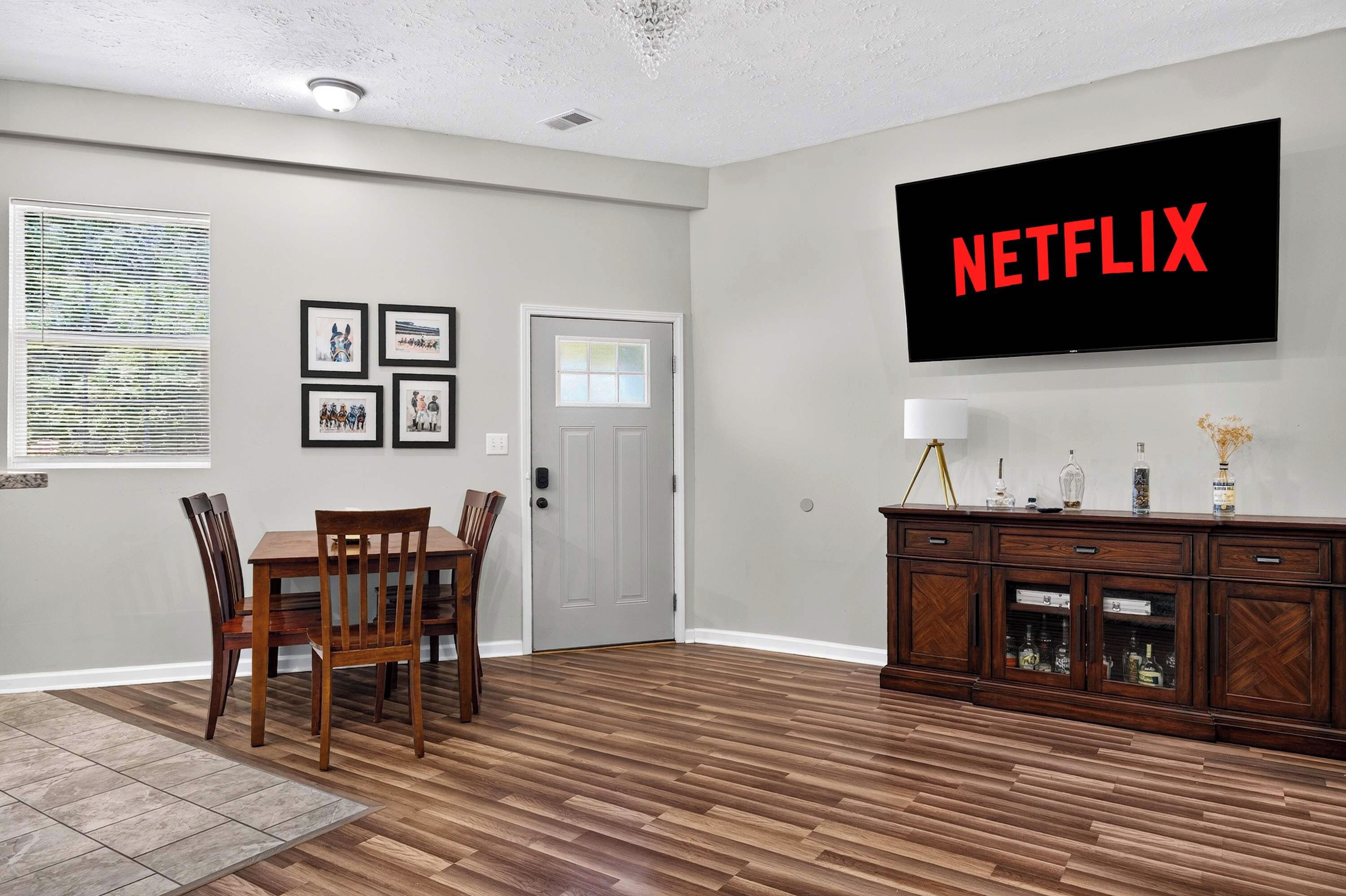 A living room with a dining area, a flat-screen TV mounted on the wall, and a wooden cabinet with decorative items.