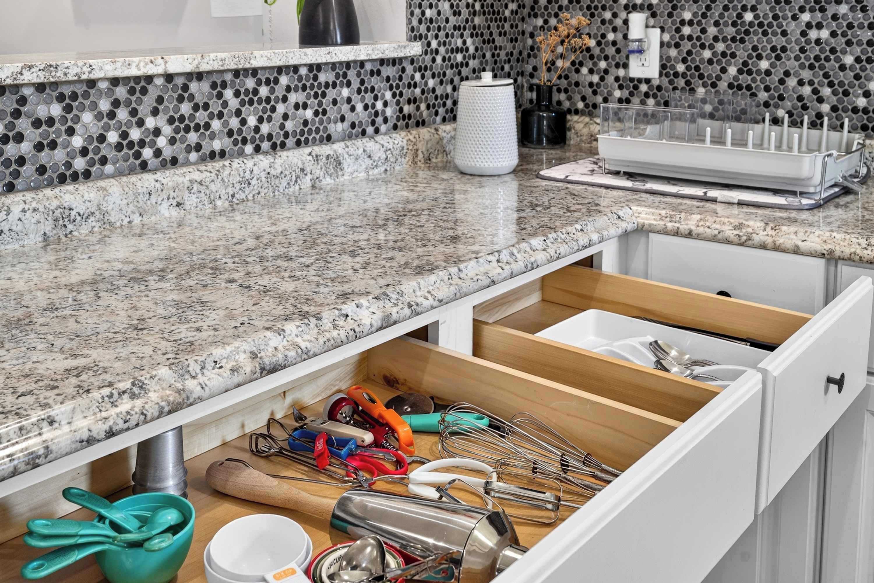 A kitchen with a granite countertop, a drawer organizer, and various kitchen utensils.