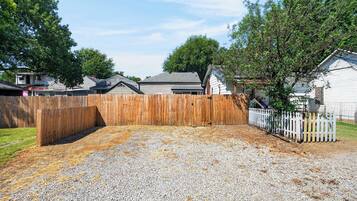 A residential backyard with a wooden fence, gravel ground, and houses in the background.
