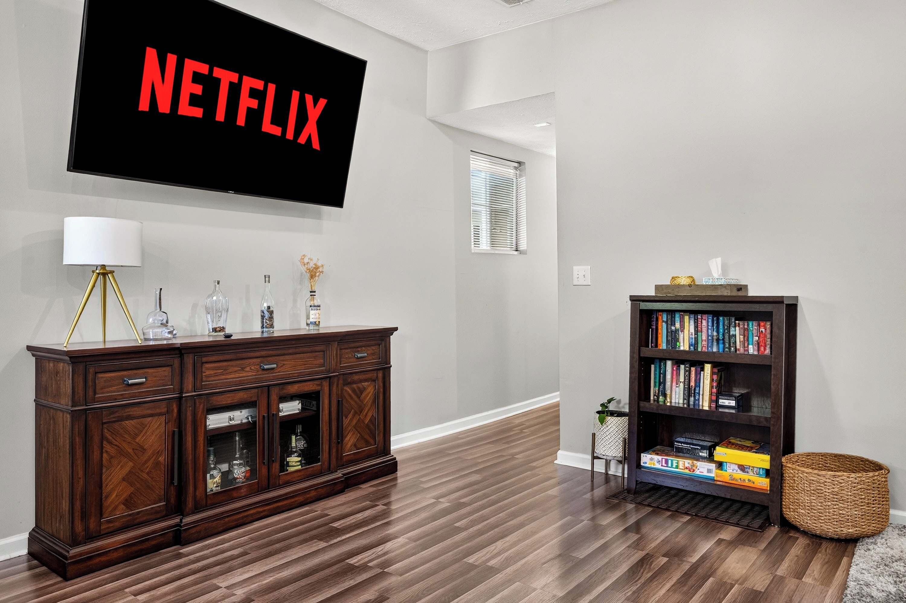 Een woonkamer met een donker houten kast, een boekenkast en een flatscreen-tv aan de muur waarop 'NETFLIX' staat.