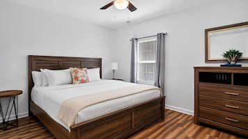 A bedroom with a wooden bed, a nightstand, a dresser, a ceiling fan, and a window with curtains.