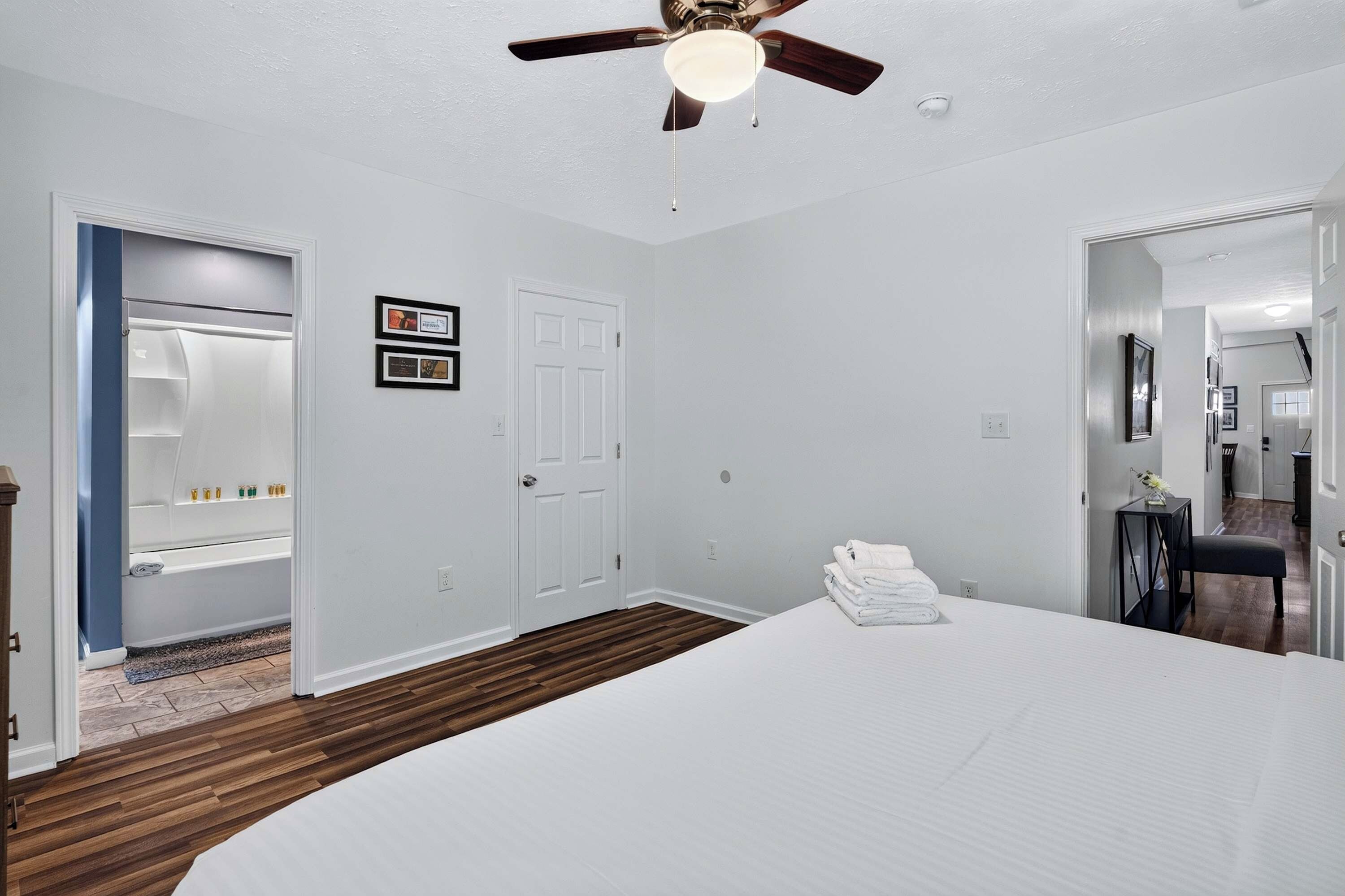 A bedroom with a bed, a ceiling fan, a door, and a small table with towels.