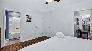 A bedroom with a bed, a ceiling fan, a door, and a small table with towels.