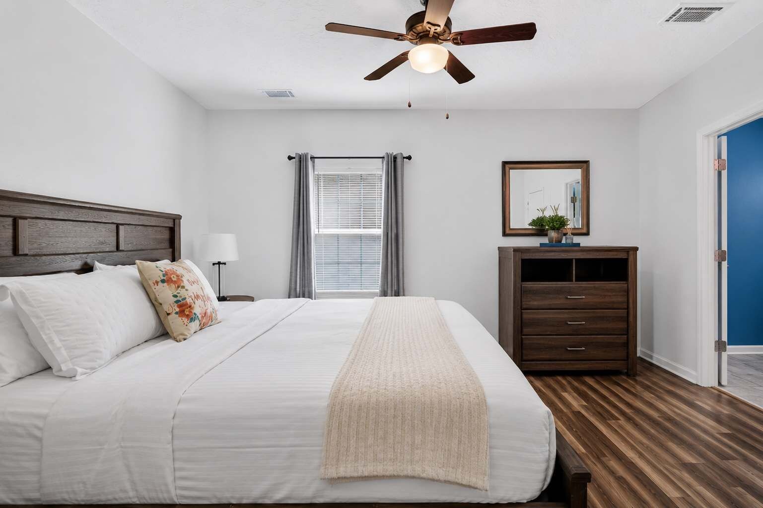 A bedroom with a bed, a ceiling fan, a nightstand, a dresser, and a window with curtains.