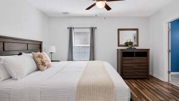 A bedroom with a bed, a ceiling fan, a nightstand, a dresser, and a window with curtains.
