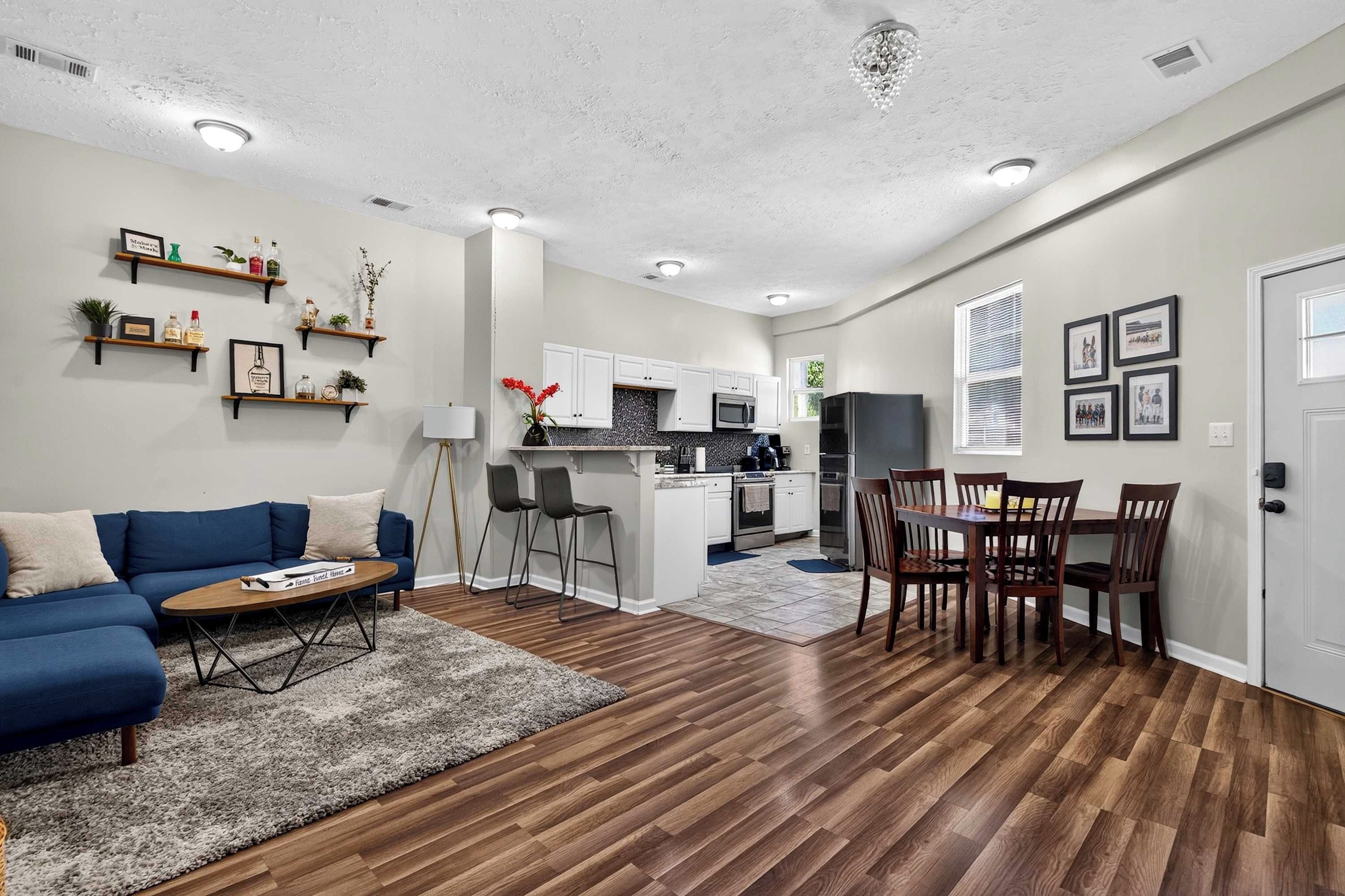 A modern living room with a blue sofa, a coffee table, and a kitchen area with white cabinets and a microwave.