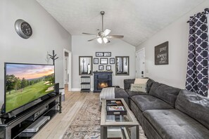 Ein Wohnzimmer mit Fernseher, Sofa, Couchtisch, Kamin und Deckenventilator.
