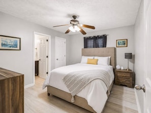 A bedroom with a bed, a ceiling fan, a nightstand, a lamp, and a door.