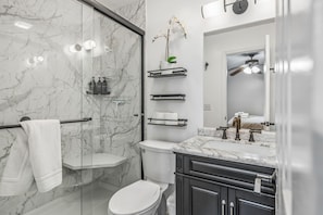 A modern bathroom with a glass shower enclosure, a toilet, a sink with a marble countertop, and a mirror above the sink.