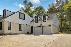 Ein zweistöckiges Haus mit Garage, überdachter Auffahrt und einem bepflanzten Garten.