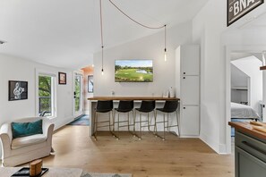 Eine moderne Küche mit Barbereich, Holzboden und einem großen Fernseher, der einen Golfplatz zeigt.